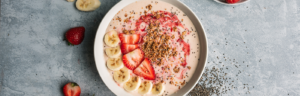 Strawberry Peanut Butter Smoothie Bowl. Sliced banana and strawberries on around the bowl, with chia seeds sprinkles on the board.
