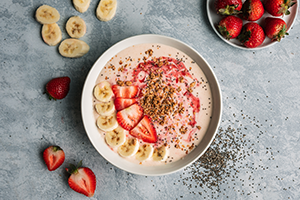 Strawberry Peanut Butter Smoothie Bowl. Sliced banana and strawberries on around the bowl, with chia seeds sprinkles on the board.